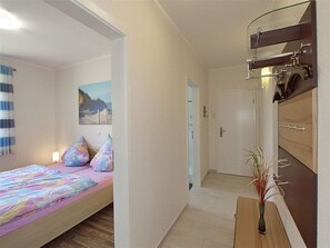 A bedroom with a bed, pillows, a bedside table with a vase, and a bathroom with a mirror and towel rack.