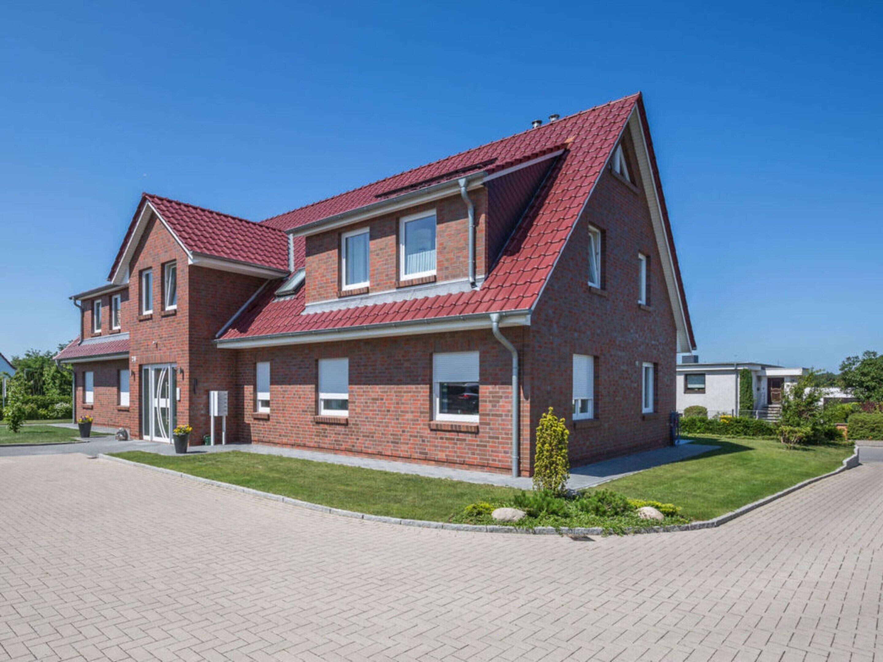 A two-story brick house with a red-tiled roof, a front entrance, and a paved driveway.