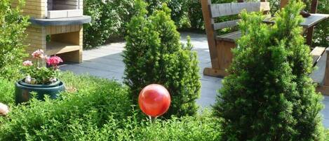 A garden area with a brick structure, possibly a barbecue or oven, surrounded by well-maintained bushes and a large red spherical object.
