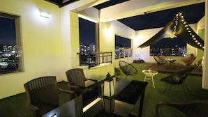 A rooftop terrace with outdoor seating, a dining table, and a view of the cityscape at night.