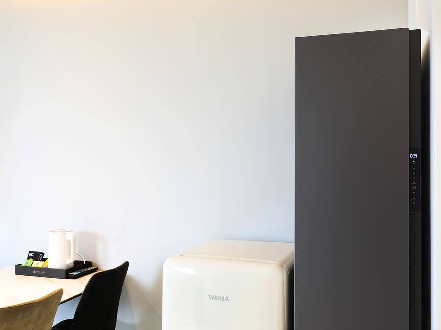 Quarto de hotel com minibar, máquina de café e geladeira preta.