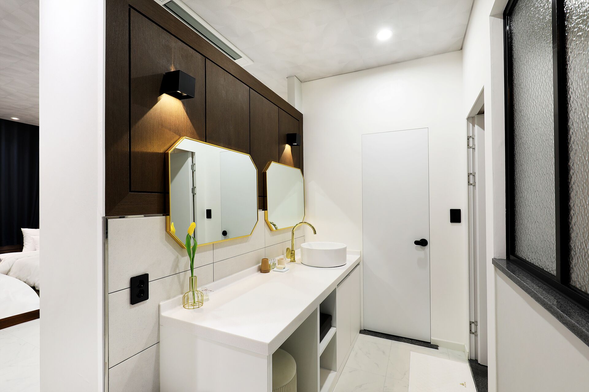 Uma casa de banho moderna com um lavatório branco, um espelho grande e uma torneira dourada.