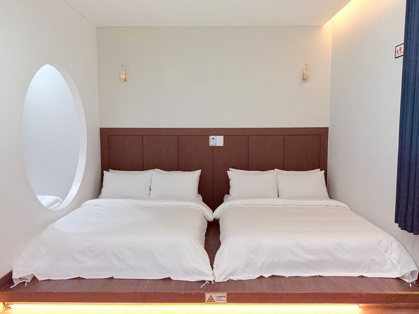 A double room with two beds, a round window, and a wooden headboard.