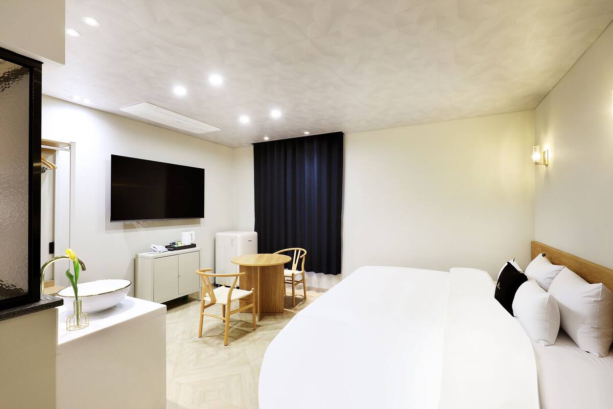 A hotel room with a bed, a desk with a chair, a TV, and a window with curtains.