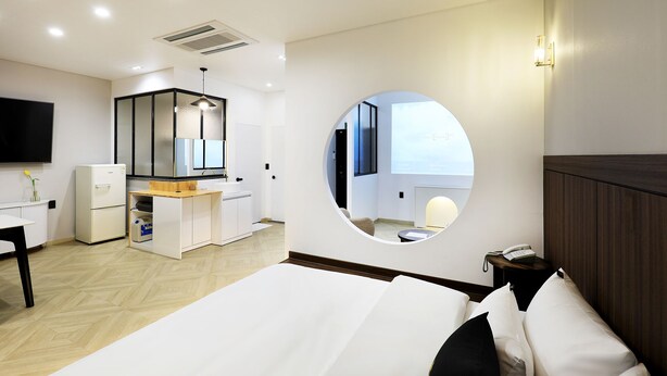 A hotel room with a bed, a desk, a mirror, a round mirror, a TV, and a view of the outside.