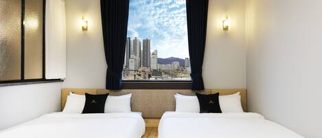 Habitación de hotel con dos camas, vista a la ciudad y dos luces fijadas a la pared.
