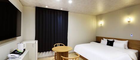 Une chambre d’hôtel comprenant un lit, un bureau avec un téléphone, une chaise, une petite table, un téléviseur et une fenêtre avec des rideaux.
