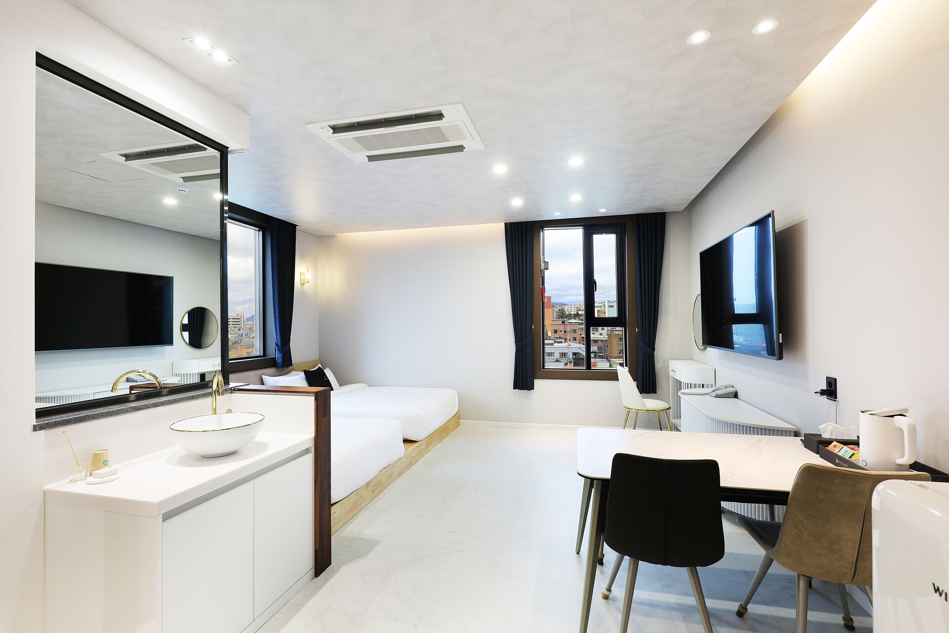 A modern hotel room with a bed, a desk, a chair, a TV, and a large window.