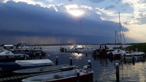 Eine Marina mit vertäuten Booten, ruhigem Wasser und einem bewölkten Himmel, durch den die Sonne bricht.