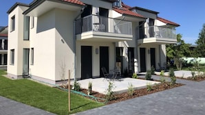Ein modernes Wohnhaus mit zwei Etagen, Balkonen, einem gepflasterten Auffahrtsweg und einem gepflegten Rasen.