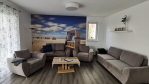 Ein Wohnzimmer mit einem Strandgemälde, zwei Sofas, einem Couchtisch und einem Fenster mit Blick.