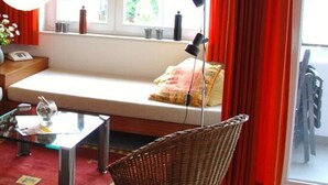 A living room with a sofa, a wicker chair, a glass coffee table, and a large window with red curtains. - Near the Beach Modern Retreat (Wangerooge)