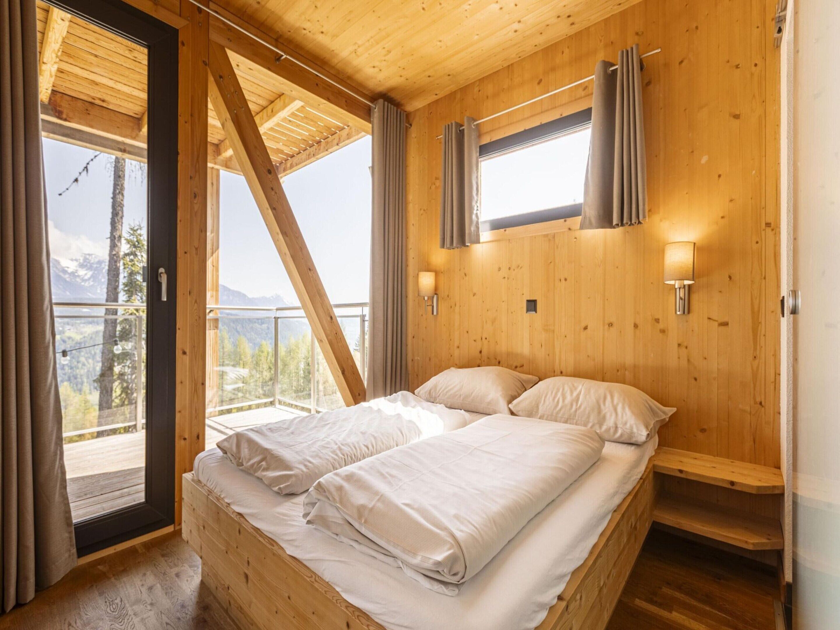Un dormitorio de madera con cama, cortinas y ventana con vistas a montañas.
