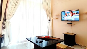 A living room with a pool table, a television mounted on the wall, and a large window with curtains.