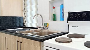 A kitchen with a stainless steel sink, a white stove, and wooden cabinets.
