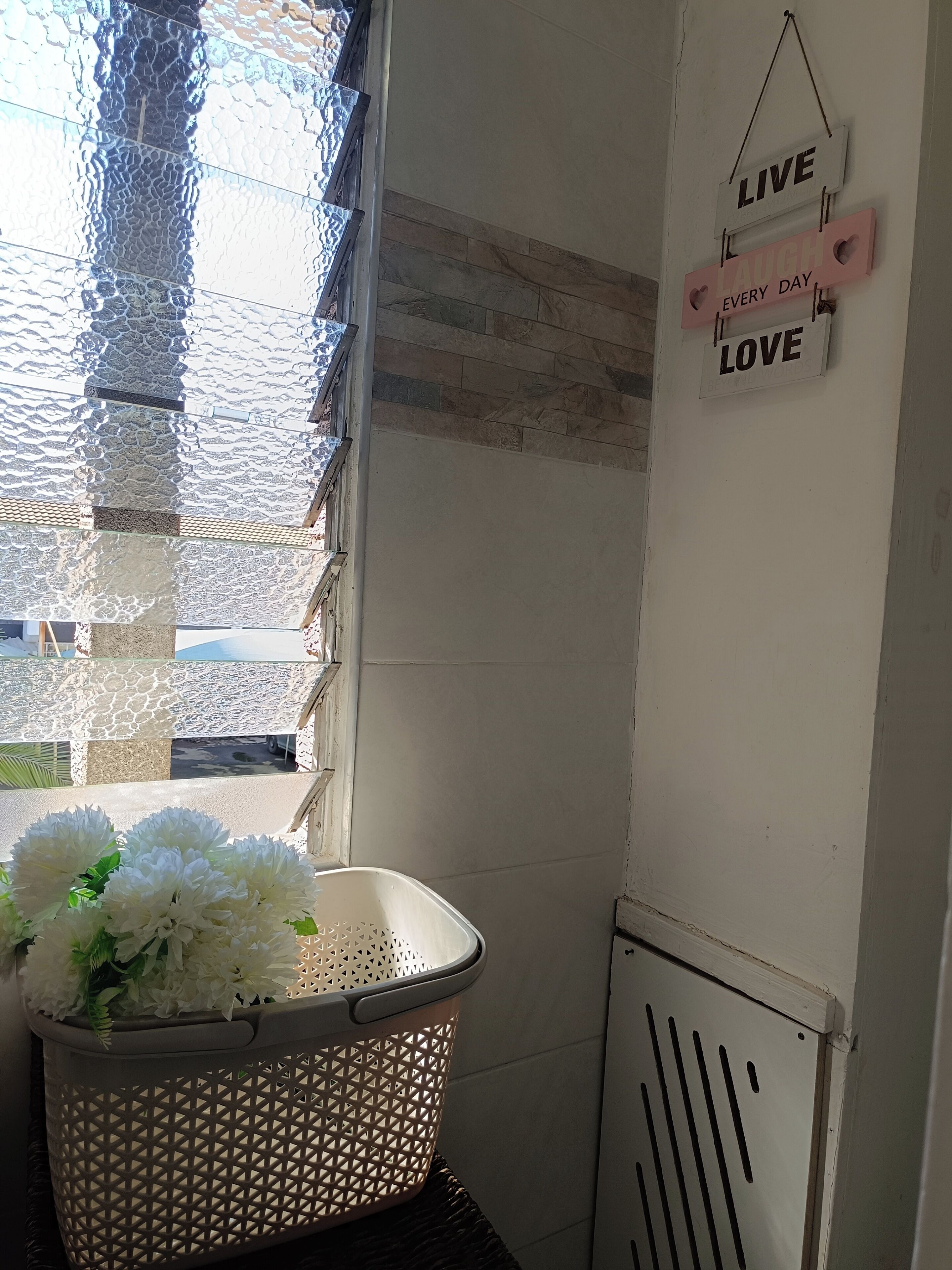 A corner of a room with a window, a basket of white flowers, and a wall with motivational signs.