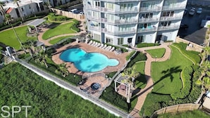 Vista aérea de um hotel com piscina central, várias varandas e jardins bem cuidados.