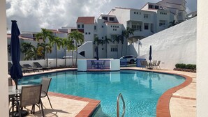 A swimming pool with a blue border, lounge chairs, and a table with chairs.
