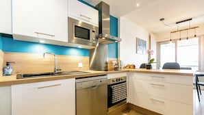 A modern kitchen with stainless steel appliances, wooden countertops, and a view of the city through large windows. - Appartement VUE MER (Quiberon)