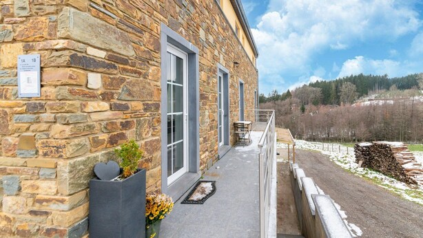 A stone building with a balcony, a small table, and chairs. There is a sign on the wall and a view of a forested area. - Family Home, Kicker, Sunset Views (Trois-Ponts)