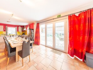 A dining area with a long table set for a meal, a kitchen area with yellow cabinets, and a view through a glass door to the outside. - Family Home, Kicker, Sunset Views (Trois-Ponts)