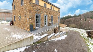 A stone building with a yellow facade, a balcony, and a view of a forested hillside. - Family Home, Kicker, Sunset Views (Trois-Ponts)