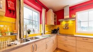 A kitchen with yellow and red walls, a stainless steel sink, wooden cabinets, and a window with curtains. - Family Home, Kicker, Sunset Views (Trois-Ponts)