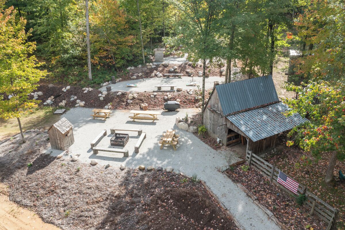 An outdoor patio area with picnic tables, a barbecue grill, and a small shed.