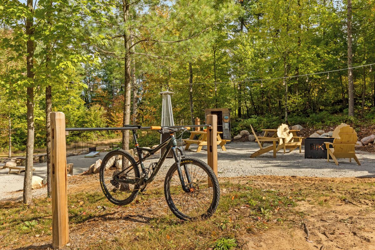 A bicycle parked near a wooden structure in a forested area with picnic tables and a grill.