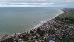 An aerial view of a coastal town with a beach, residential areas, and a road leading to the sea.