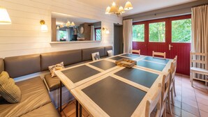 Un comedor con una mesa larga, sillas de madera, un banco y una puerta roja que da al exterior.