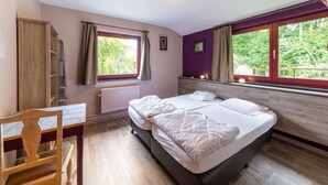 Un dormitorio con dos camas, un escritorio y una ventana con vistas a árboles.