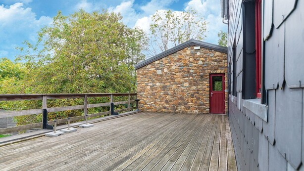 Una terraza de madera con un edificio de piedra y una puerta roja.