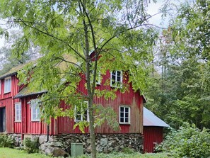 A red wooden house with a stone foundation, surrounded by lush greenery. - 4 Star Holiday Home in Tvaaker (Tvaaker)