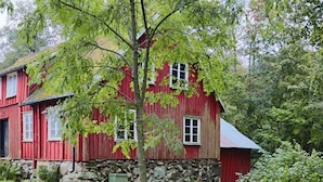 A red wooden house with a stone foundation, surrounded by lush greenery. - 4 Star Holiday Home in Tvaaker (Tvaaker)