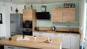 A modern kitchen with a stainless steel refrigerator, a built-in oven, a microwave, a wooden countertop, a sink, and a television above the cabinets. - T3 au Calme Proche Paris (Fontenay-sous-Bois)