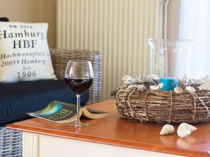 A wooden table with a glass of red wine, a book, and a decorative basket with stones and a candle. - Holiday Apartment Reet Domicile (Hage)