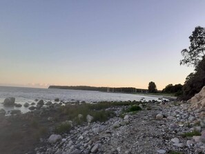 A rocky shoreline with a calm body of water, trees, and a distant landmass. - 6 Person Holiday Home in Stubbekobing (Stubbekobing)