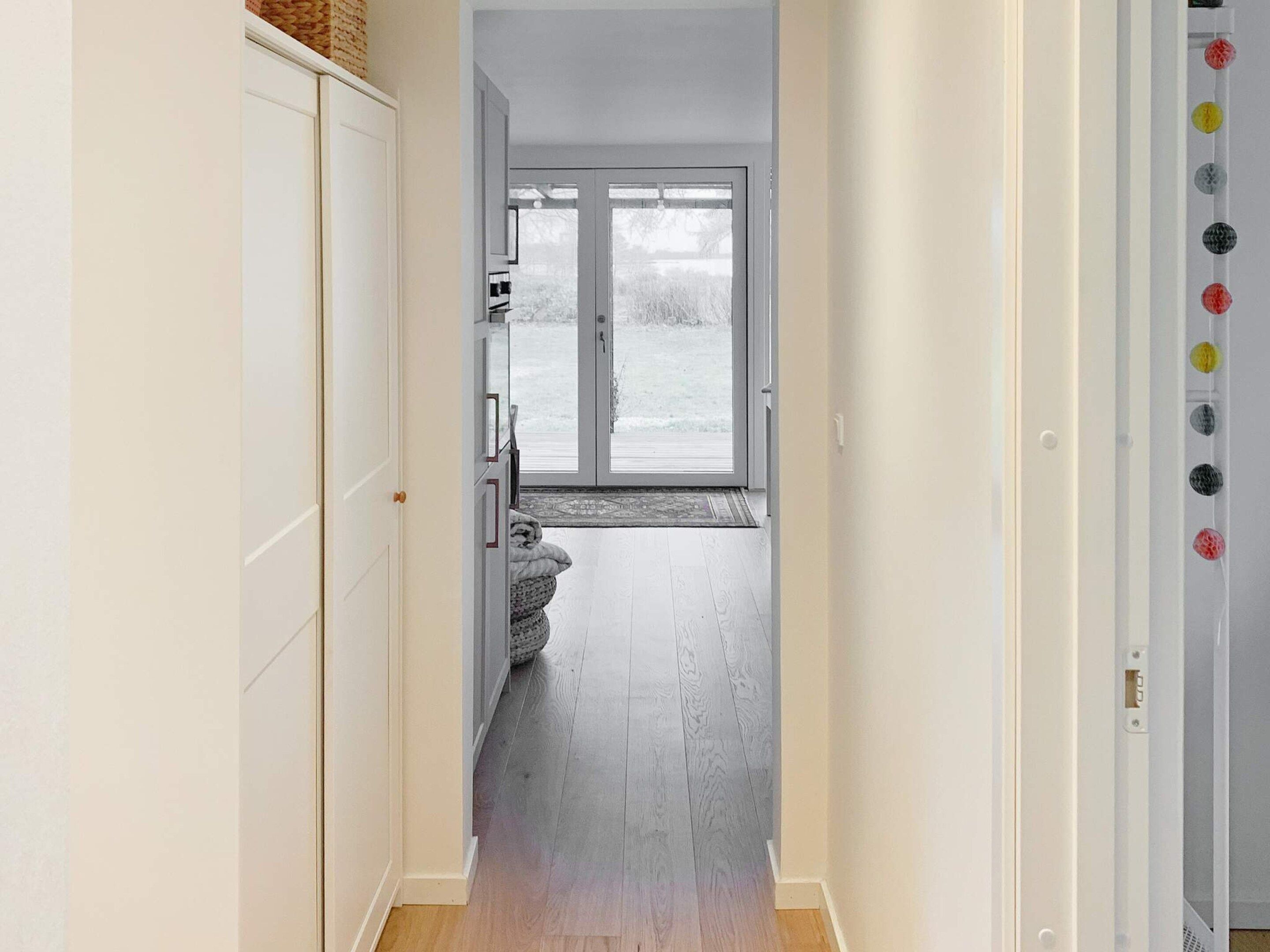 A hallway leading to a room with a sliding glass door, a white wardrobe, and a door with a handle.