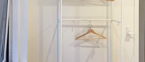 A white closet with two wooden hangers on a rod, a black shelf, and a white decorative item.