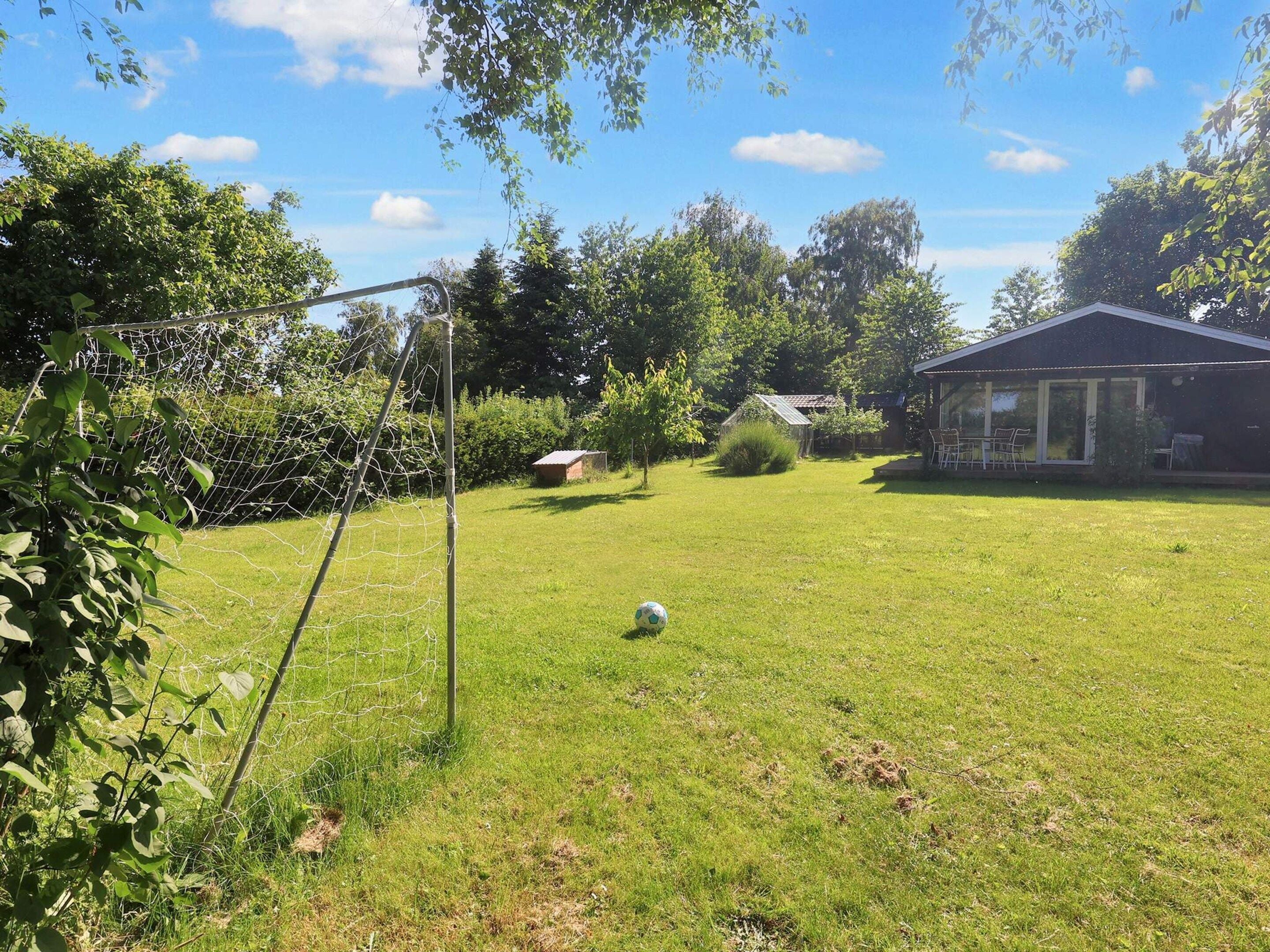 A grassy outdoor area with a soccer goal, a small shed, and a house with a patio.
