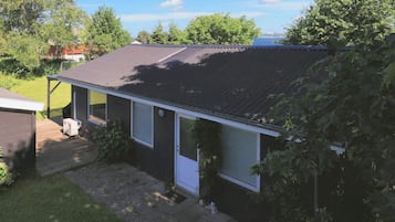 A single-story house with a dark roof, a small porch, and a visible air conditioning unit.