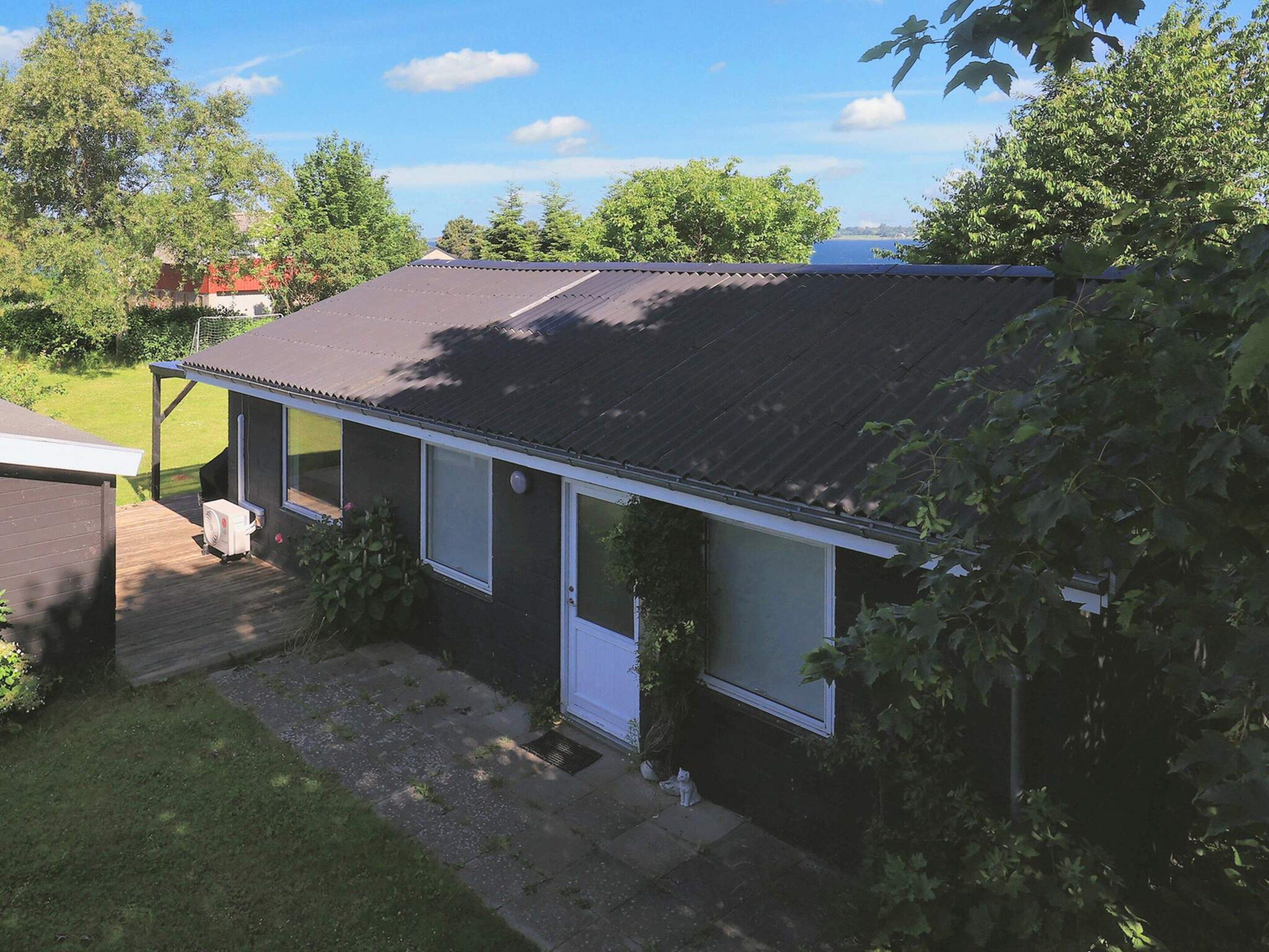 A single-story house with a dark roof, a small porch, and a visible air conditioning unit.