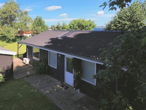 A single-story house with a dark roof, a small porch, and a visible air conditioning unit. - 6 Person Holiday Home in Stubbekobing (Stubbekobing)