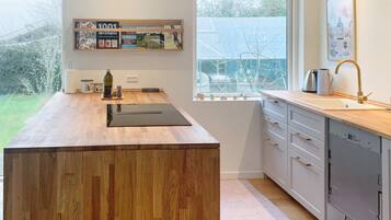 A modern kitchen with a wooden countertop, a built-in oven, and a window with a view of greenery.