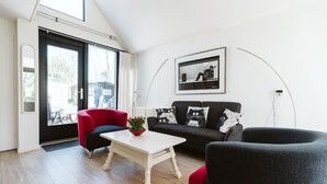 Una sala de estar con un sofá negro, un sillón rojo, una mesa de centro blanca y un cuadro en blanco y negro colgado en la pared.