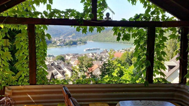 A wooden bench and table inside a covered area with a view of a lake and town. - Multicultural Comfortable Holiday Residence (Kamp-Bornhofen)