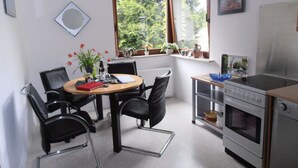 A compact kitchen with a dining area, featuring a round table, chairs, a stove, and a window with a view of greenery. - Multicultural Comfortable Holiday Residence (Kamp-Bornhofen)