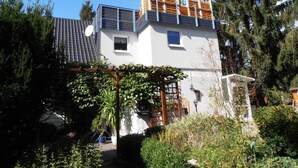 A two-story building with a white facade, a satellite dish, and a wooden deck on the upper floor. - Multicultural Comfortable Holiday Residence (Kamp-Bornhofen)