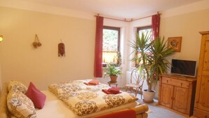 A bedroom with a bed, a chair, a TV, a cabinet, and a window with curtains. - Multicultural Comfortable Holiday Residence (Kamp-Bornhofen)